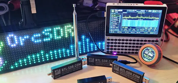 My bench: the OrcSDR LED sign, a telescopic antenna and RTL-SDR Blog V4L, V3c and V4 dongles in front of an M5Stack Tab5 with its keyboard running OrcSDR at 15.680 MHz, and an M5Stack Dial showing the same frequency